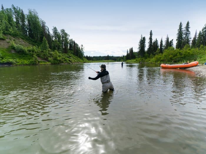 Female angler throws a fishing line into a flowing creek in Alaska on a Kings and Corn summer excursion.