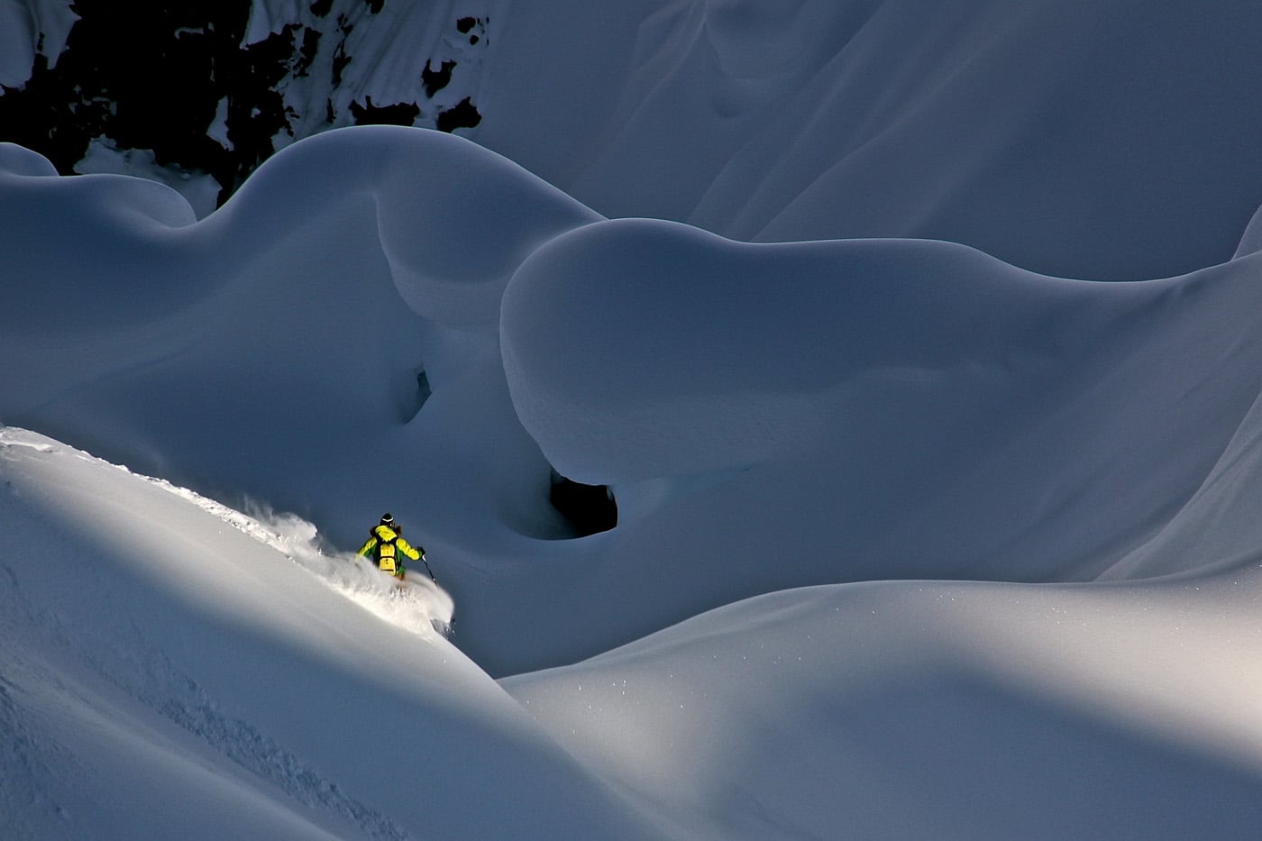 Skier in a yellow and black snowsuit navigates between two snow-covered cliffs.