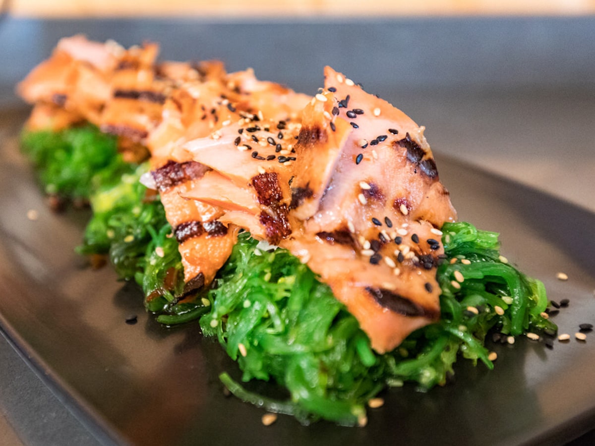 A close up of a plate of Alaska salmon on a bed of greens.