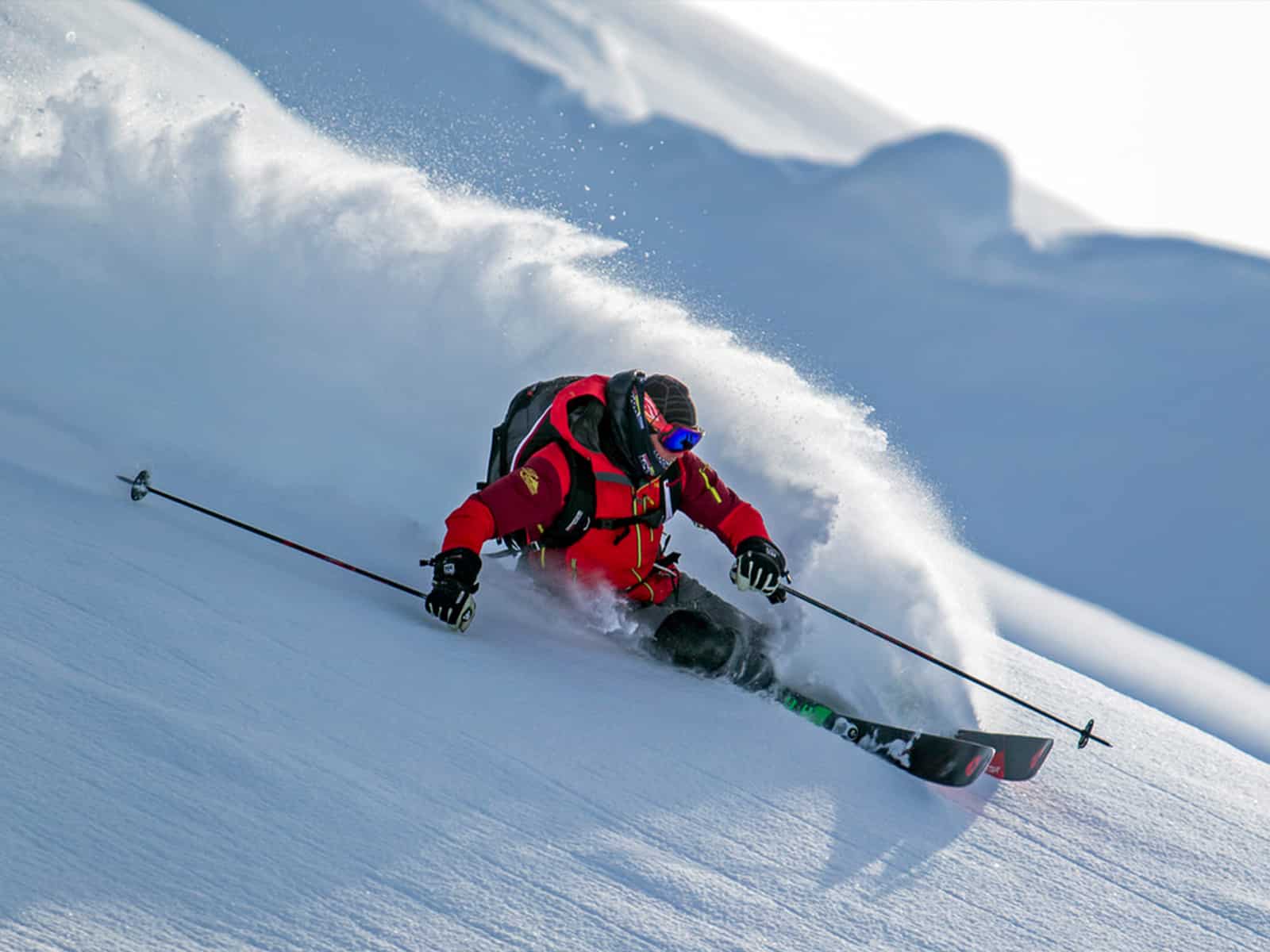 Close up of a skier going down a mountain with a cloud of snow behind him.