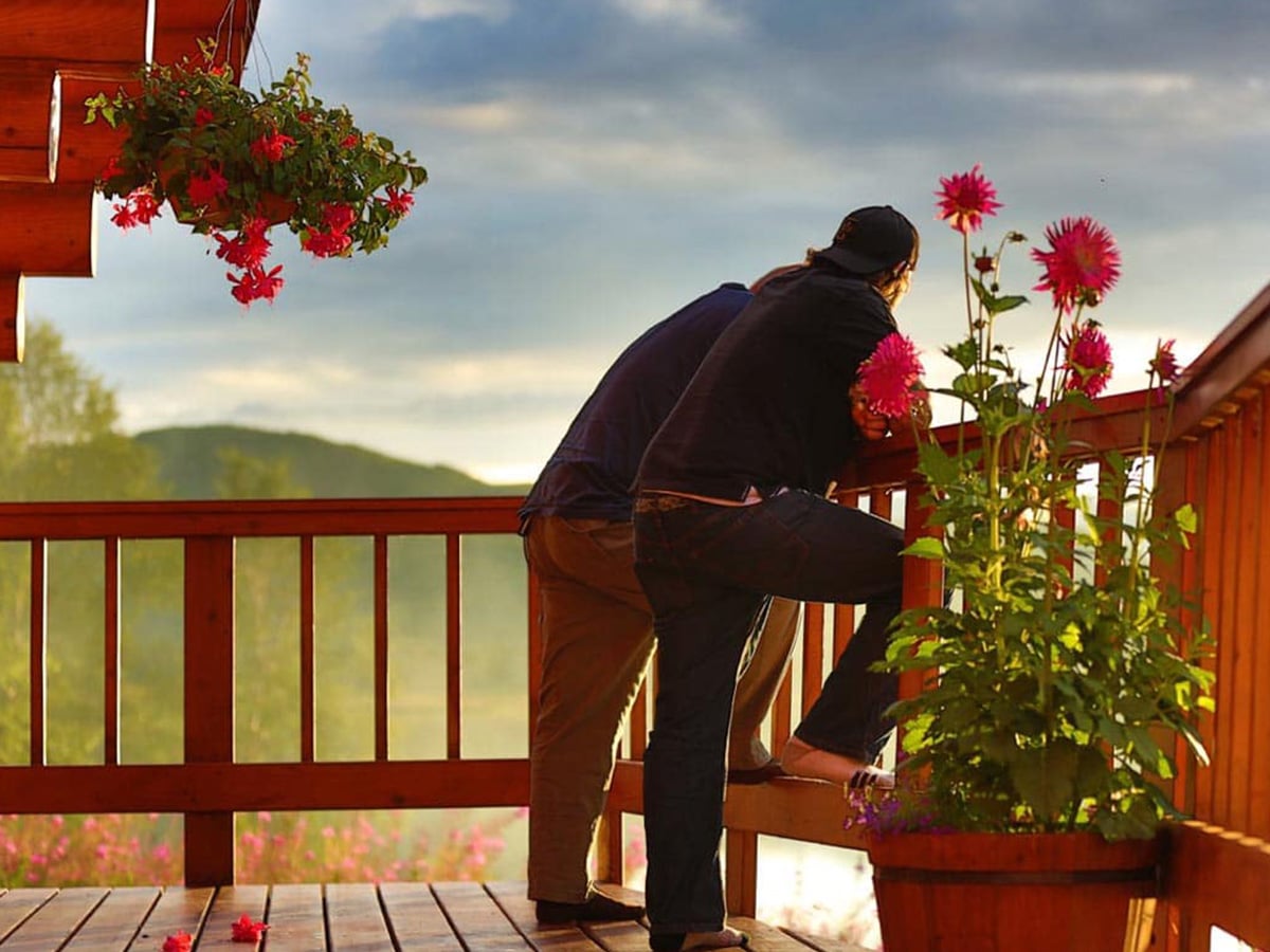 Two men standing outside on the Tordrillo Mountain Lodge balcony on a sunny day.