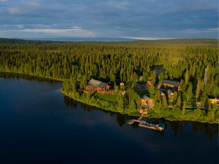 Panoramic view of Tordrillo Mountain Lodge cabins nestled in the woods next to a body of water.