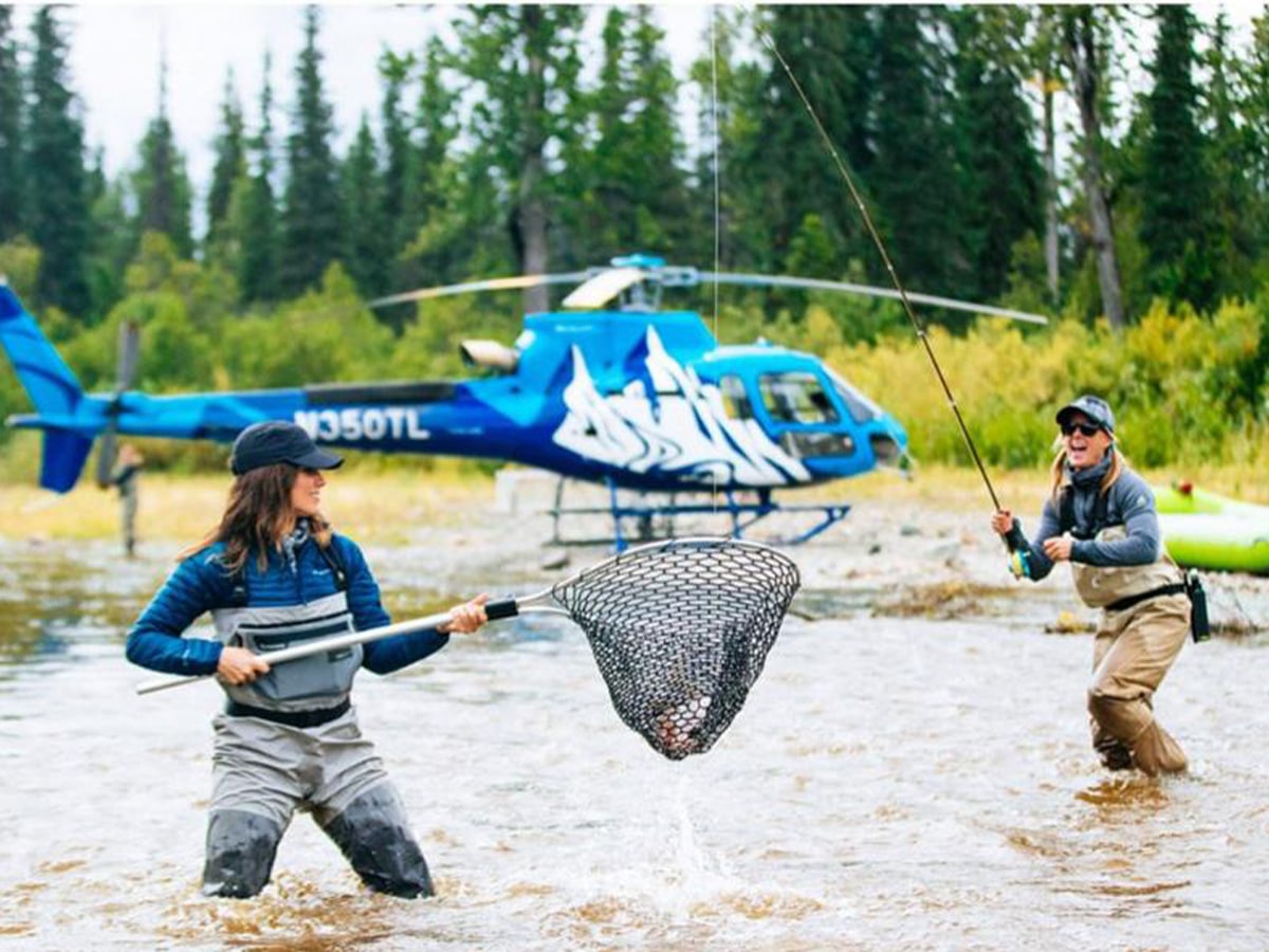 Two women fishing for salmon with a helicopter in the background.