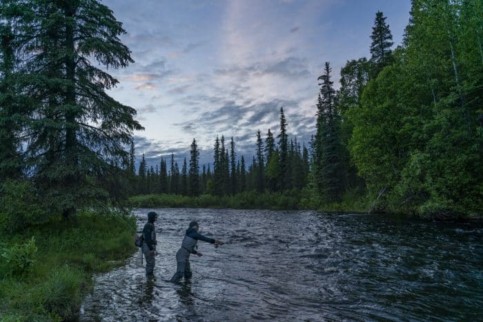 A freshwater creek with two fishermen casting their lines while fishing in Alaska.