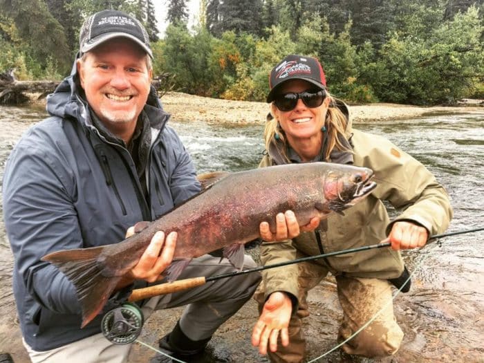 Two Tordrillo Mountain Lodge guests hold a salmon they caught next to a river.