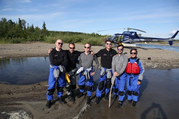 A group stands in front of a helicopter after a whitewater rafting excursion in Alaska.