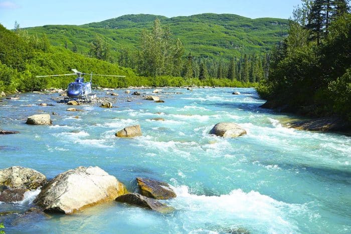 A helicopter flies over a freshwater river and heads towards a whitewater rafting spot in Alaska.