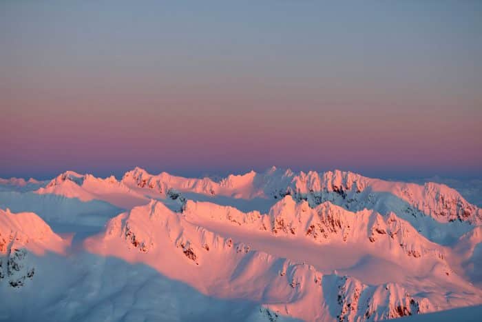 Aerial view of a pink sunset over snow-covered mountain tops in Alaska.