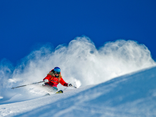 Female skier in a red coat and goggles skis down a mountain of fresh powder.