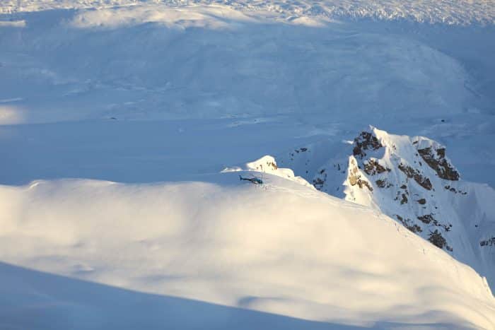 Aerial view of a blue helicopter dropping off heli skiers on a mountaintop in Alaska.