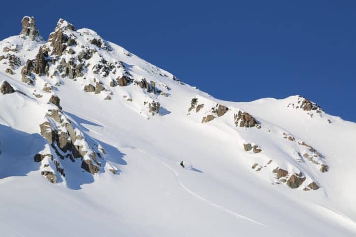 A single snowboarder glides down a mountain in Alaska while on a snowboarding tour with Tordrillo Mountain Lodge.