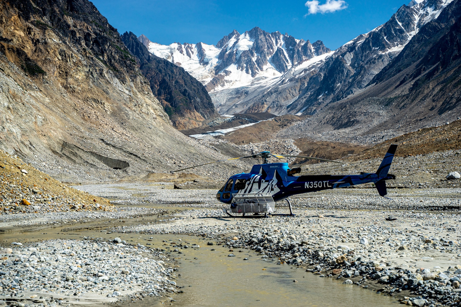 a helicopter sits in a valley within the tordrillo mountains after taking clients hiking