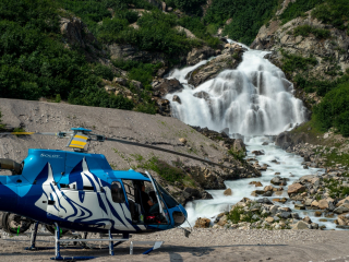 a helicopter and its pilot sits under a waterfall in the tordrillo mountains