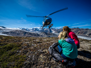 two people wait for a helicopter pickup while hiking in the Tordrillo Mountains