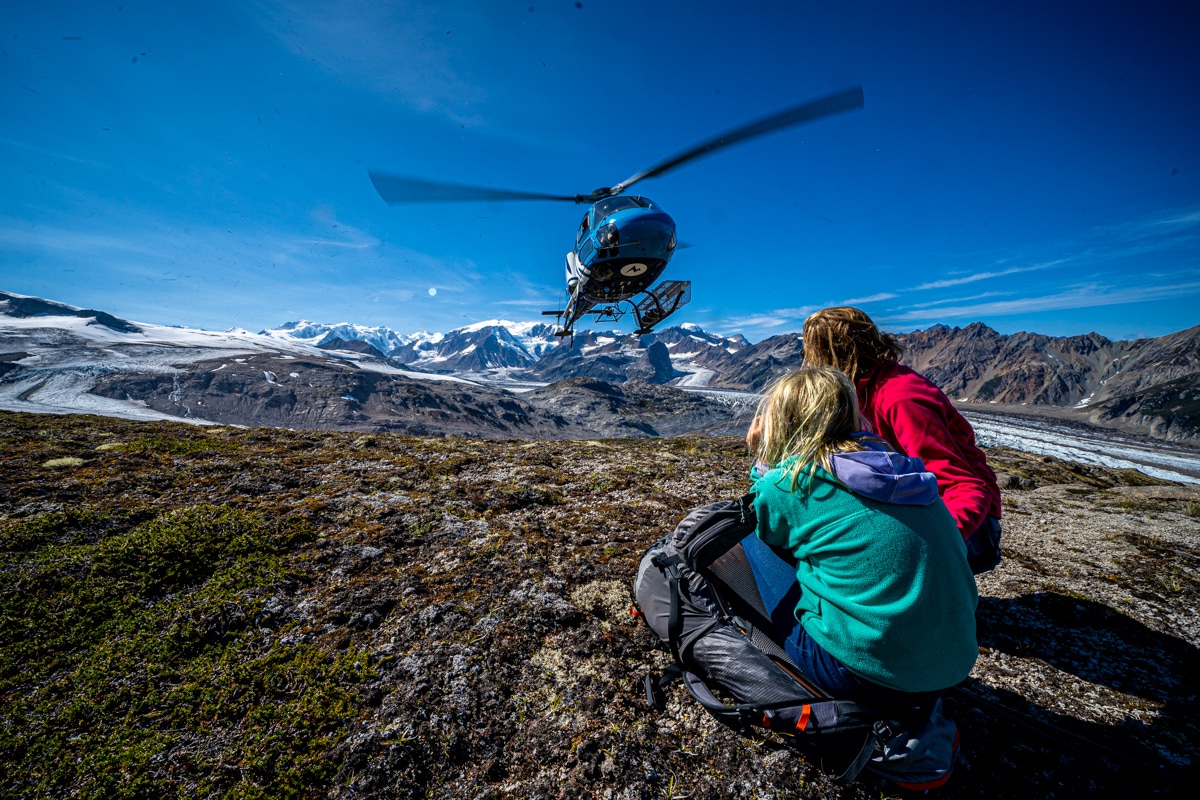 two people wait for a helicopter pickup while hiking in the Tordrillo Mountains