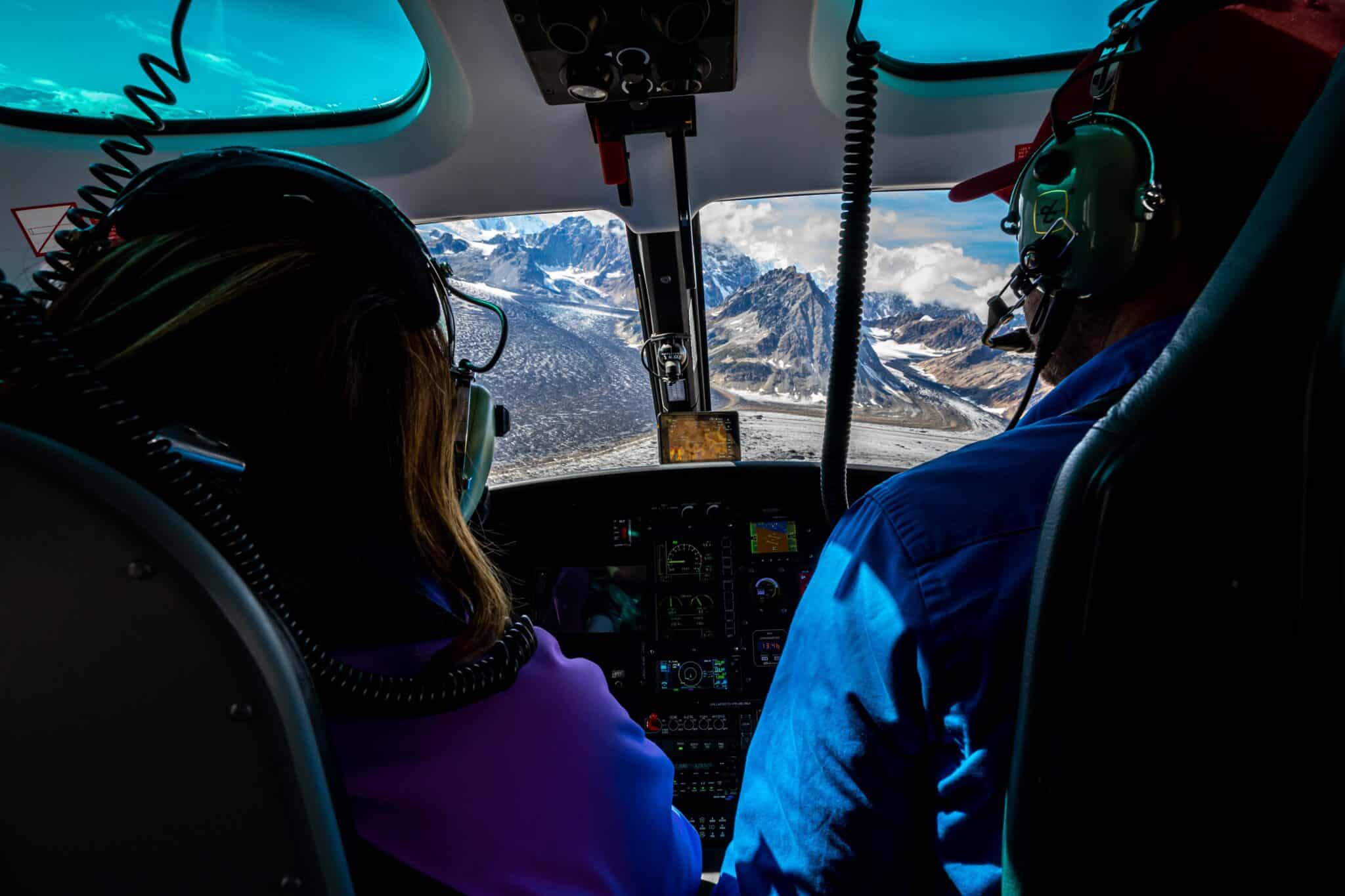 a passenger and pilot fly in a helicopter above the triumvirate glacier