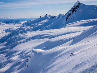 Heli snowboarder navigates a snow-covered valley with mountains in Alaska.